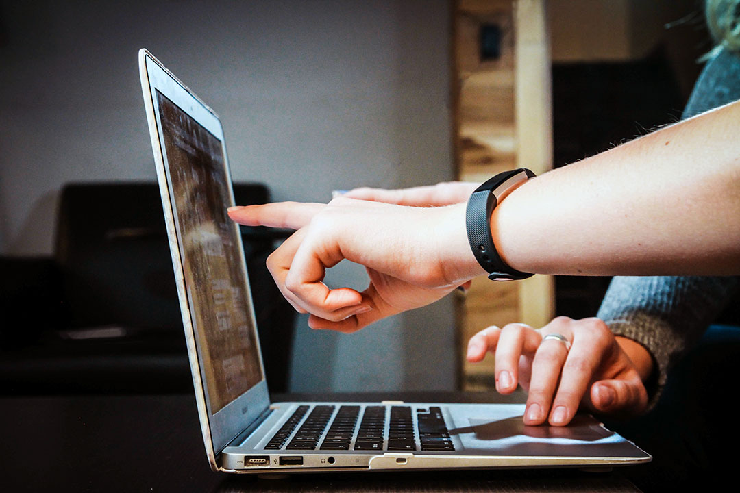 Three hands with one pointing to laptop screen indicating help